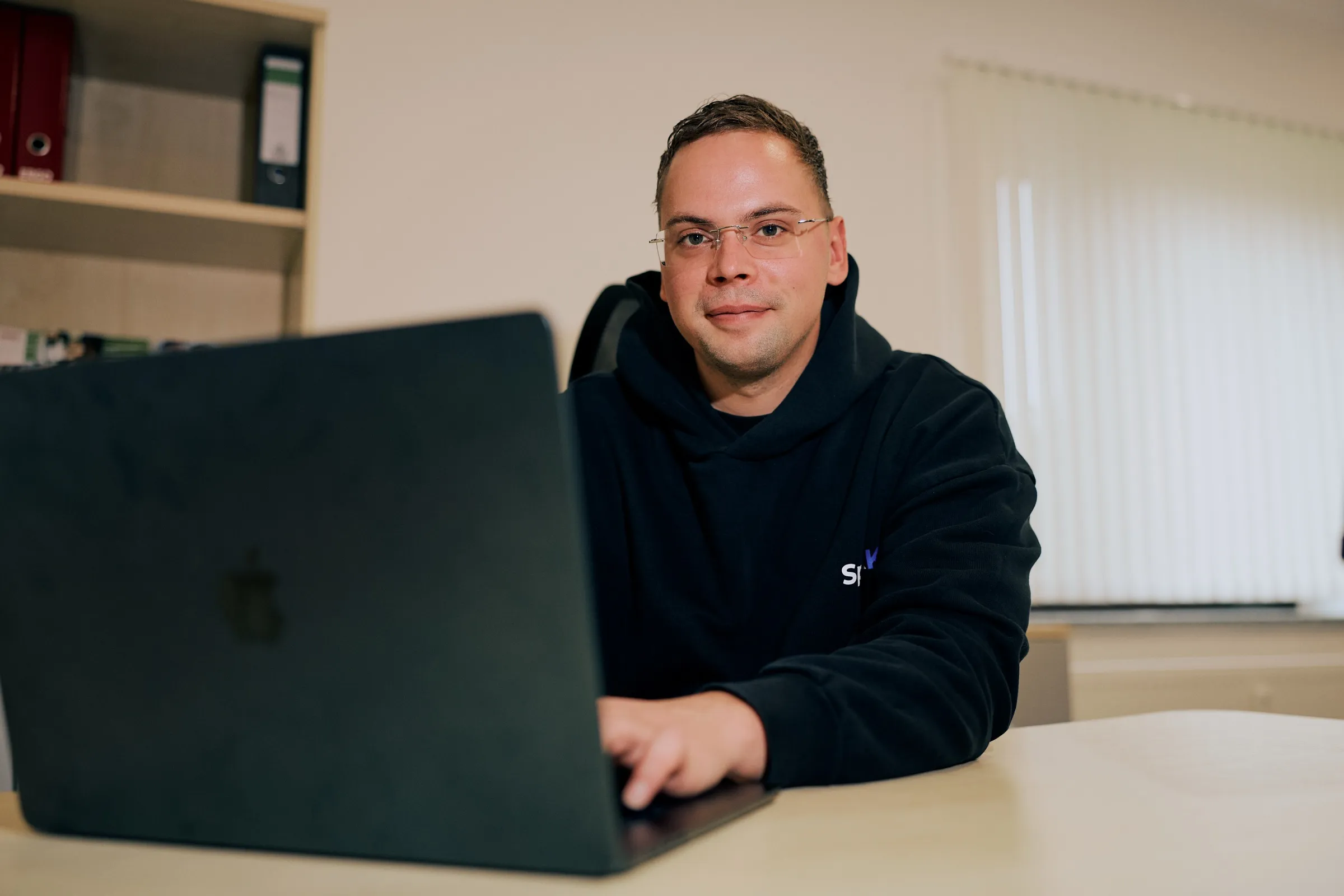Felix Denker sitzt lächelnd am Laptop im SpeakKI-Büro