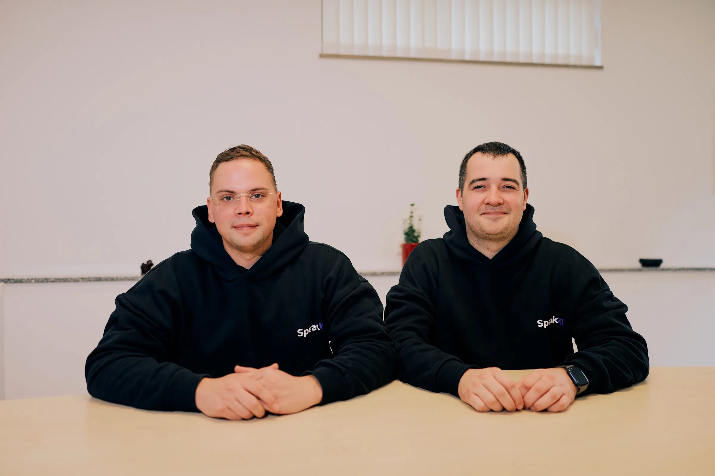 Felix Denker und Marvin Ludwig, die Gründer von SpeakKI, sitzen nebeneinander an einem Tisch im Büro in Rodenkirchen
